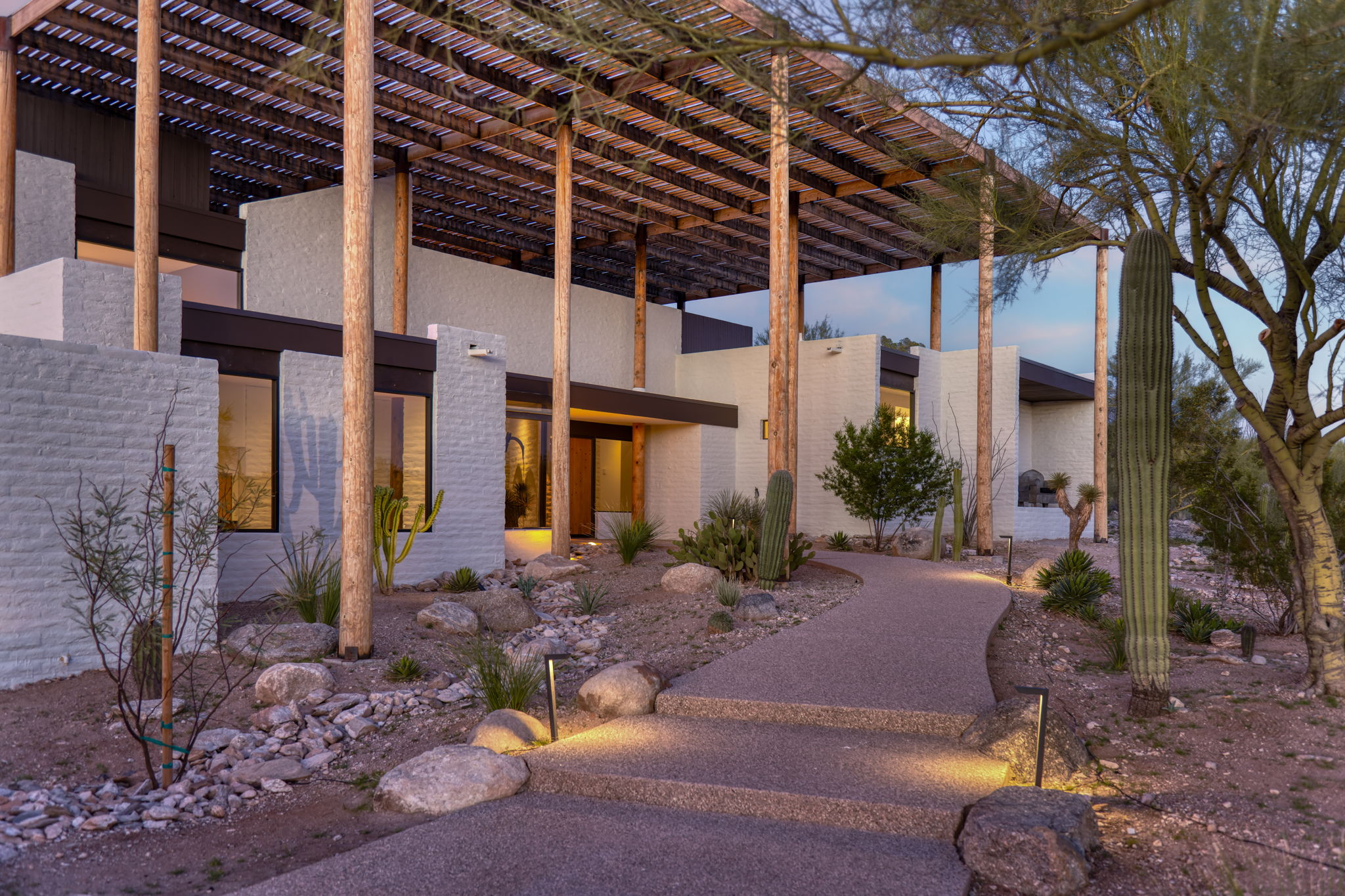 The Ramada House by Judith Chafee at blue hour — the wood lattice canopy on round timber posts shading the white masonry block house below.
