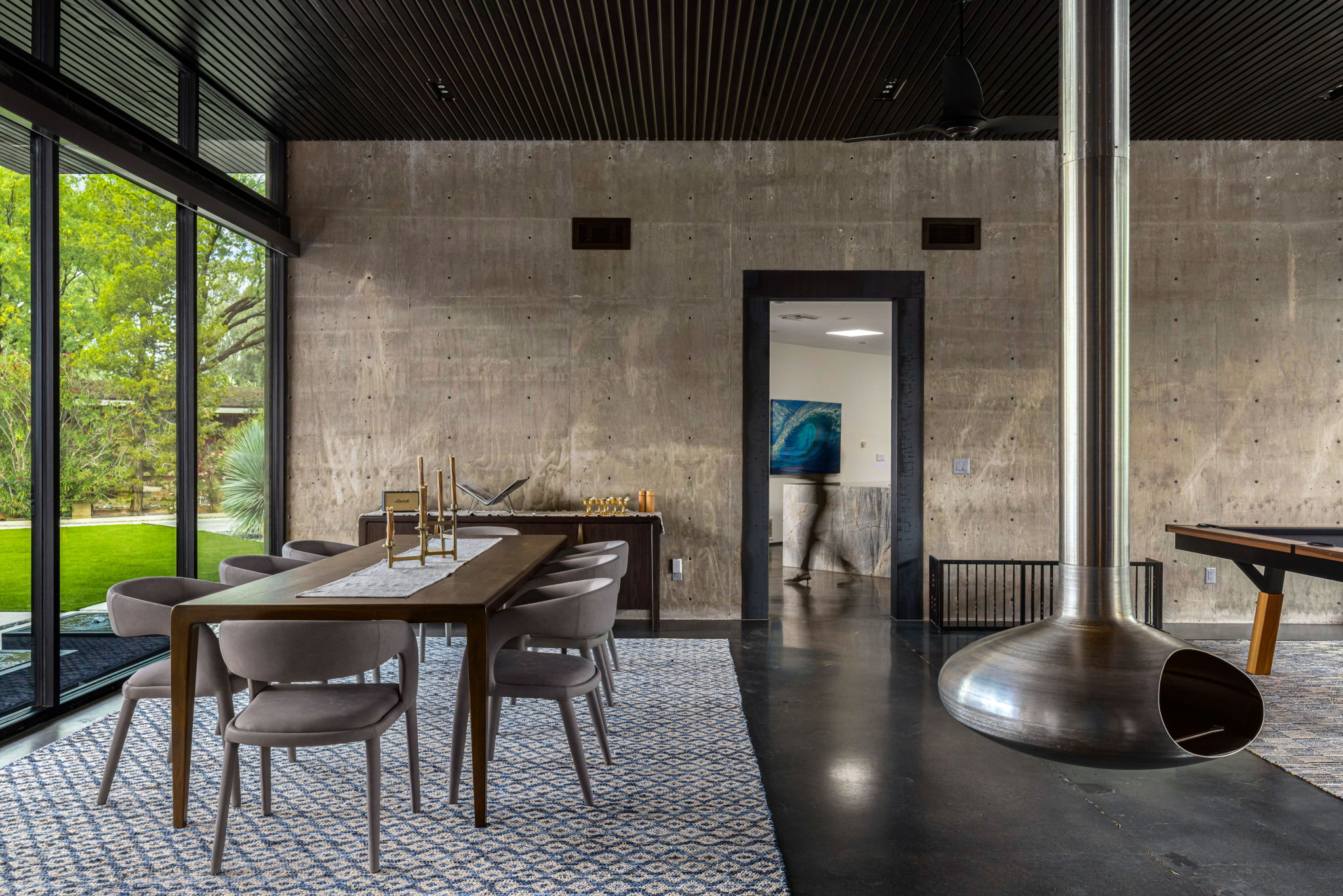 The dining room at the Country Club Estates home — a wood table with chairs, the suspended steel chimney visible at right, and a figure in motion blur passing through a doorway in the back wall.