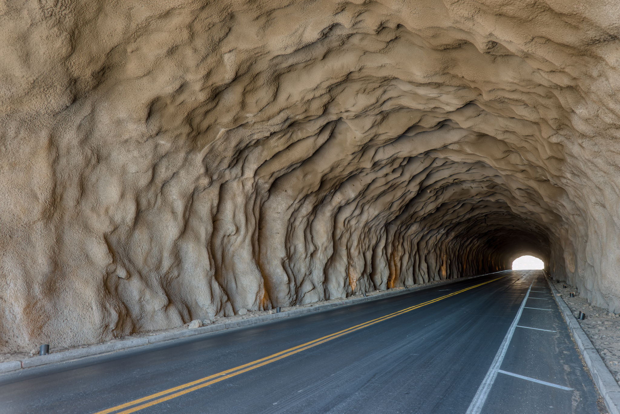 Inside the Saguaro Ranch tunnel &mdash; sculpted sandstone walls and ceiling worked into organic waves, the road receding toward a bright oval of desert light at the far end.